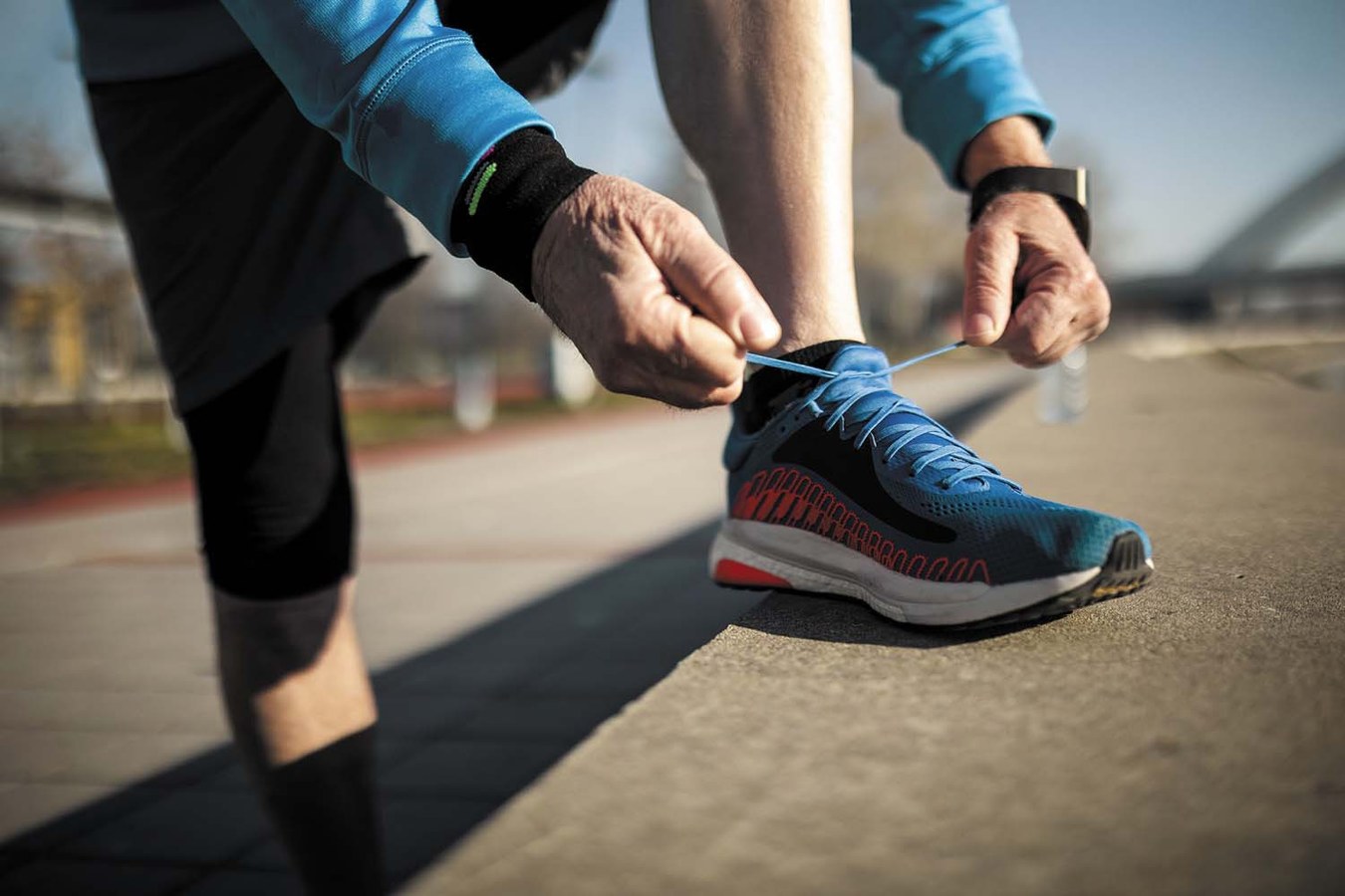 cropped photo showing the arms and lower body of a man with one foot on a concrete wall tying his running shoe